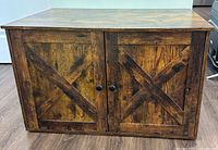 Front view of a wooden cabinet with double barn door style doors, showing rustic brown finish and black knob handles.