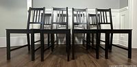 Front view of eight black wooden dining chairs arranged in two rows