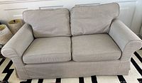Front view of IKEA Upplands loveseat showing two seat cushions and two back cushions in light beige upholstery with rolled arms.
