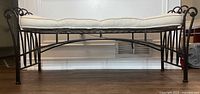 Side view of black iron bench showing full length and cushion on top