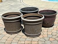 Four large plastic outdoor planters on a paved surface near a pool, showing size and overall appearance