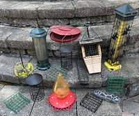 Wide view of assorted bird feeders showing different designs, materials, and sizes, placed on stone steps.