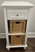 Front view of white nightstand showing drawer and two wicker baskets.