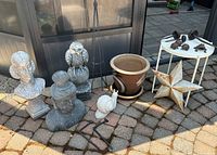 Full view of outdoor garden décor including busts, owl sculpture, snail sculpture, planter, metal star, plant stand and small metal animals.