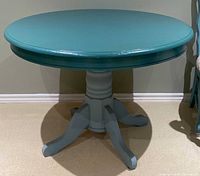 Front view of wooden round blue pedestal dining table showing table top and base with curved legs.
