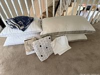 Photo of king size pillows stacked and folded sheet sets on beige carpet showing color and fabric details.