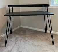 Front view of black wood and metal retro desk showing hairpin legs and riser shelf.