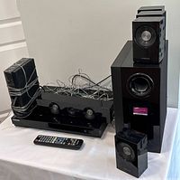 Full surround system setup including central unit, subwoofer, four satellite speakers, remote control, and cables