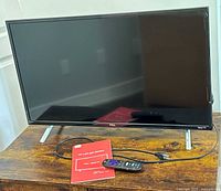 Angled view of TCL 32-inch Roku TV showing front, remote, power cord, and manual.