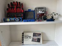 Wide view of assorted tools on shelf showing screwdriver set, Mastercraft level, Husky stubby tool set, magnifying clamp, and closed Precision Knife Set box.