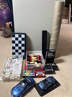 Overview photo showing all items from the lot including chess/checkerboard, dominoes, Jenga blocks, Cards Against Humanity, Harry Potter wand, puzzle roll, and blue model cars.