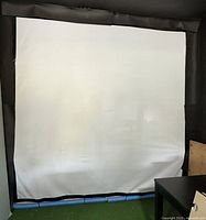 Front view of the 9x9 white virtual golf simulator screen with black border attached to a frame, showing the entire screen surface from floor to ceiling.