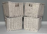 Four white square wicker baskets stacked in two rows showing outer weave and handles.