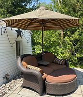 Front view of two-seat wicker lounge sofa, ottoman and umbrella on patio