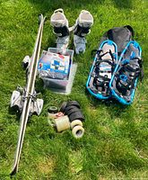 Wide view of all items in the lot on grass showing skis, boots, snowshoes, sporting tape, and accessories.