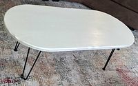 Side angle view of wooden coffee table with white scalloped top and black hairpin legs, showing overall shape and condition.