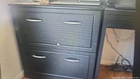 Front view of black wooden storage cabinet with two spacious drawers with silver metal handles, minor surface scratches visible.