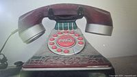 Photo showing vintage Coca-Cola rotary dial telephone in dark red with silver accents and Coca-Cola logos on dial and base.