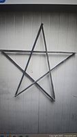 Metal star constructed from five stakes arranged to form a large five-point star, photographed against a wooden panel background.