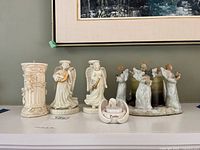 Porcelain angel candle holders setup including pedestal candle, two angels with instruments, tea light holder, and group of four angels around candles