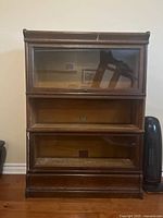 Front view of three-section barrister bookcase showing glass drop-front doors on upper two sections and open bottom section