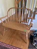 Front three-quarter view of wooden bench showing curved spindle back, arms, and turned legs.