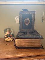 Wide view showing stacked vintage Bibles with gold embossed covers and Nativity Christmas snow globe on wooden surface under window light.