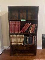 Front view of modern four shelf bookshelf filled with various hardcover books but offered empty.