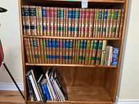 Full view of two bookshelves. Top two shelves contain Encyclopaedia Britannica Great Books volumes with gold-embossed leather-like spines in multiple colors. Lower shelf has assorted books with mixed formats and colors.