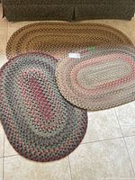 Three small oval braided rugs grouped on floor showing color and pattern variations