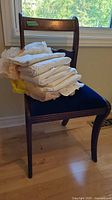 Antique wooden chair with royal blue velvet seat with stack of vintage lace linens placed on it.