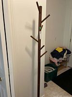 Full view of the wood coat tree standing upright against a white wall, showing multiple pegs and reaching 66 inches tall.