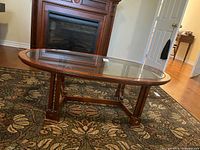 Oval wooden coffee table with glass top on a patterned rug, showing full top and leg design.
