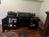 Full view of the wooden desk showing two cabinets with shelves and drawers, with top surface holding a printer and other office equipment (not included). Left cabinet door and right drawer are open.