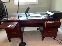 Full frontal view of the solid wood desk with glass top, showing drawer arrangements and contents on top which are not included.