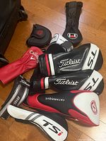 Photo of various golf club head covers from Titleist, Callaway, Odyssey, Kataraqi brands on a wooden floor.