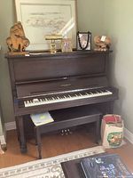 Full view of the Heintzman upright piano with bench underneath and various decorative items on top, including a brass desk lamp and wooden sculptures.