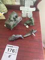 Photo of the full lot showing the translucent Inuksuk, green seal, bear on rock, kayak with paddle, and two dolphin carvings all displayed on a wooden surface.