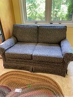 Front view of blue floral two-seater loveseat, showing fabric pattern and overall condition including wear and skirted bottom.