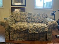Front view of two-seater love seat sofa with floral cushions and skirted base in living room setting.