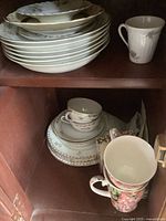 Stack of white plates and bowls on top shelf. Vintage floral cups and matching saucers on bottom shelf, with two larger floral cups.
