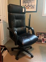 Full view of black leather office chair showing slight wear on the seat front edge and padded backrest with headrest.
