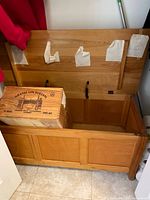 Open pine storage bench showing the interior and hinged lid with some wear and fabric tape remnants on the underside of the lid. Wine crate placed inside.