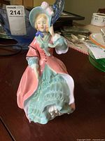 Front view of Royal Doulton Spring Morning figurine in pink and green with hat, showing detail and cracks in porcelain.