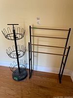 Black metal circular three-tier shoe stand with round basket racks and black base next to a wood slat towel rack with black metal frame.