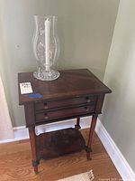 Full view of wooden side table with glass candle holder on top containing white candle, showing table front and top surface.