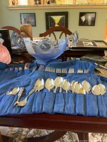 Silverplate flatware pieces including spoons and forks organized in blue felt wrap on dining table.