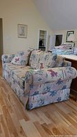 Side view of floral sofa showing rolled arm and skirted base, cushions, and matching accent pillows.