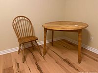 Wooden dining table with folding ends and a wooden spindle back chair next to it on wooden floor against beige walls.