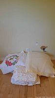 Duvet cover, floral pillow sham, knit blanket, and folded sheets on floor against wall